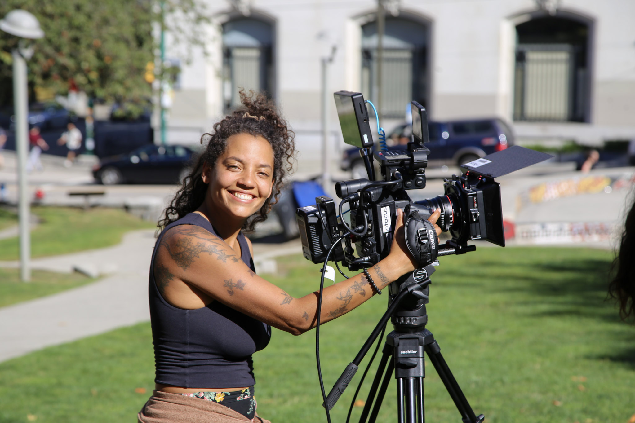 Student smiling behind a camera on a tripod while shooting outdoors